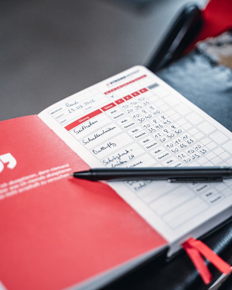 Ausgefüllte Doppelseite mit Übungen, Wiederholungen und Gewichten, daneben ein Stift.