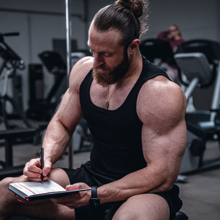 Athlet trägt im Studio seine Sätze in das StrongNotes® Trainingsbuch ein.