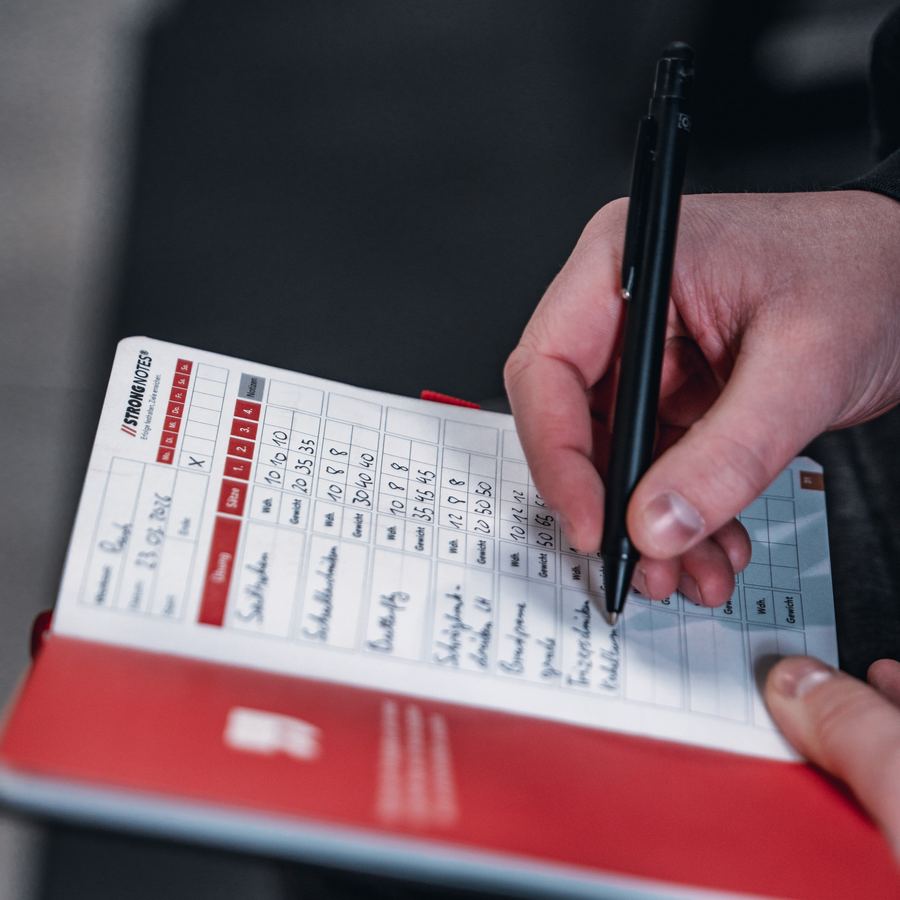 Hand mit Stift trägt Gewichte und Wiederholungen in die Doppelseite ein.