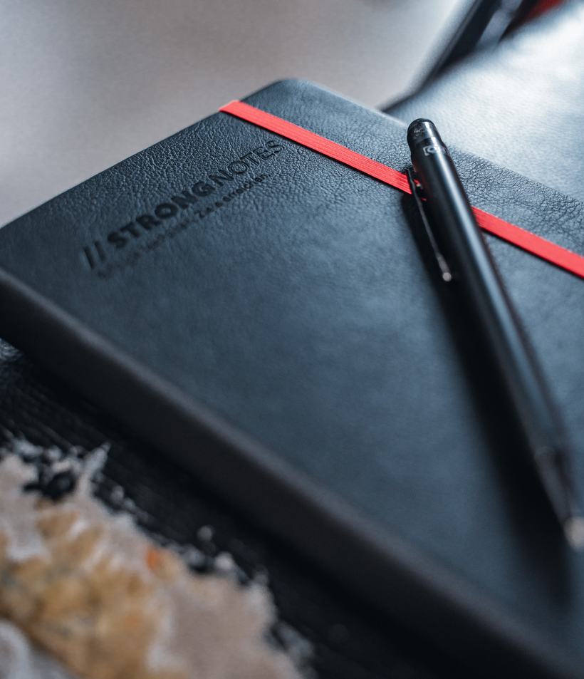 Nahaufnahme des Covers mit fühlbarer Blindprägung, rotem Gummiband und Stift.